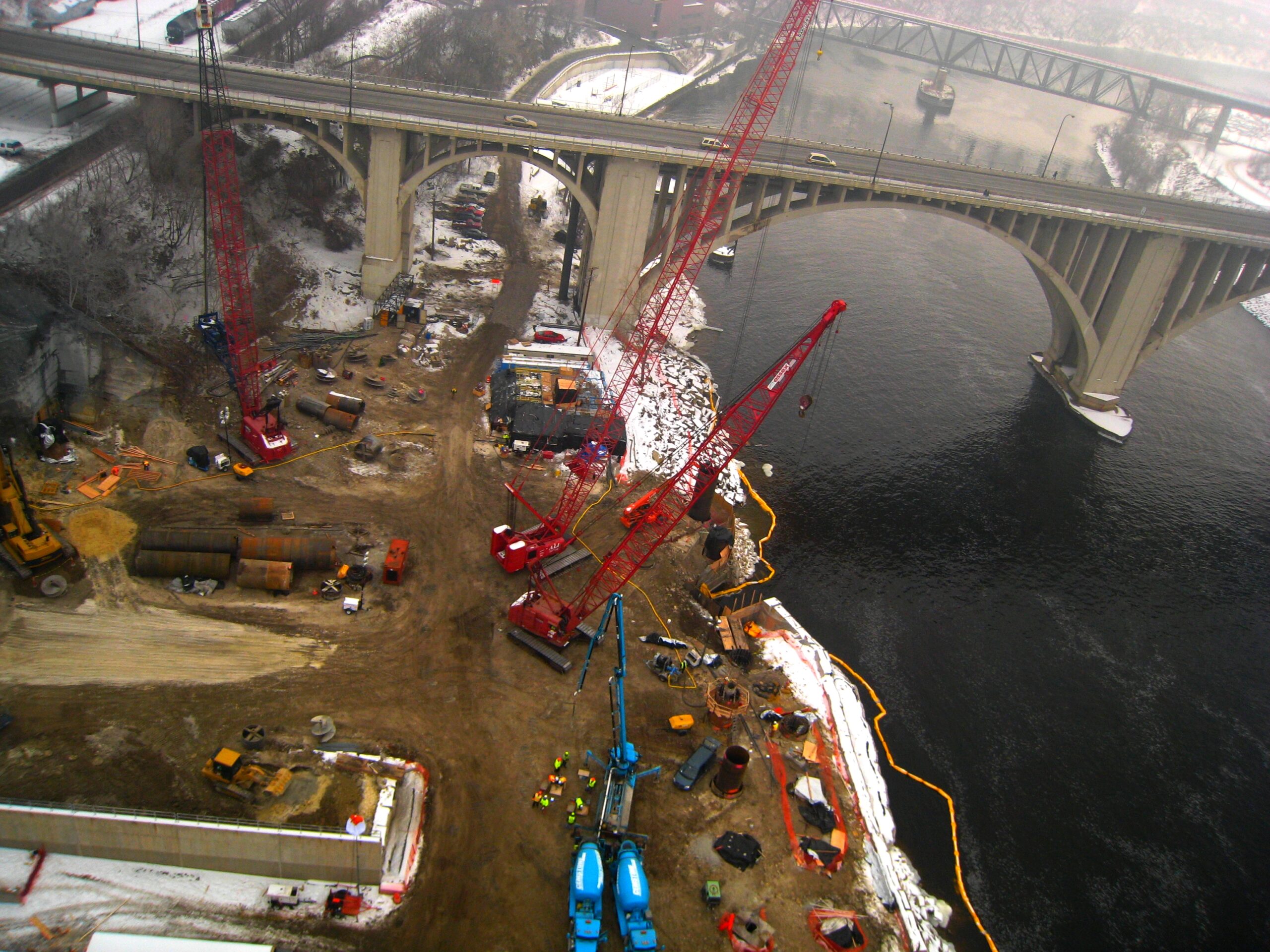 Cranes, a concrete pump and ready mixed trucks at the I-35W Bridge construction site beside the Mississippi River