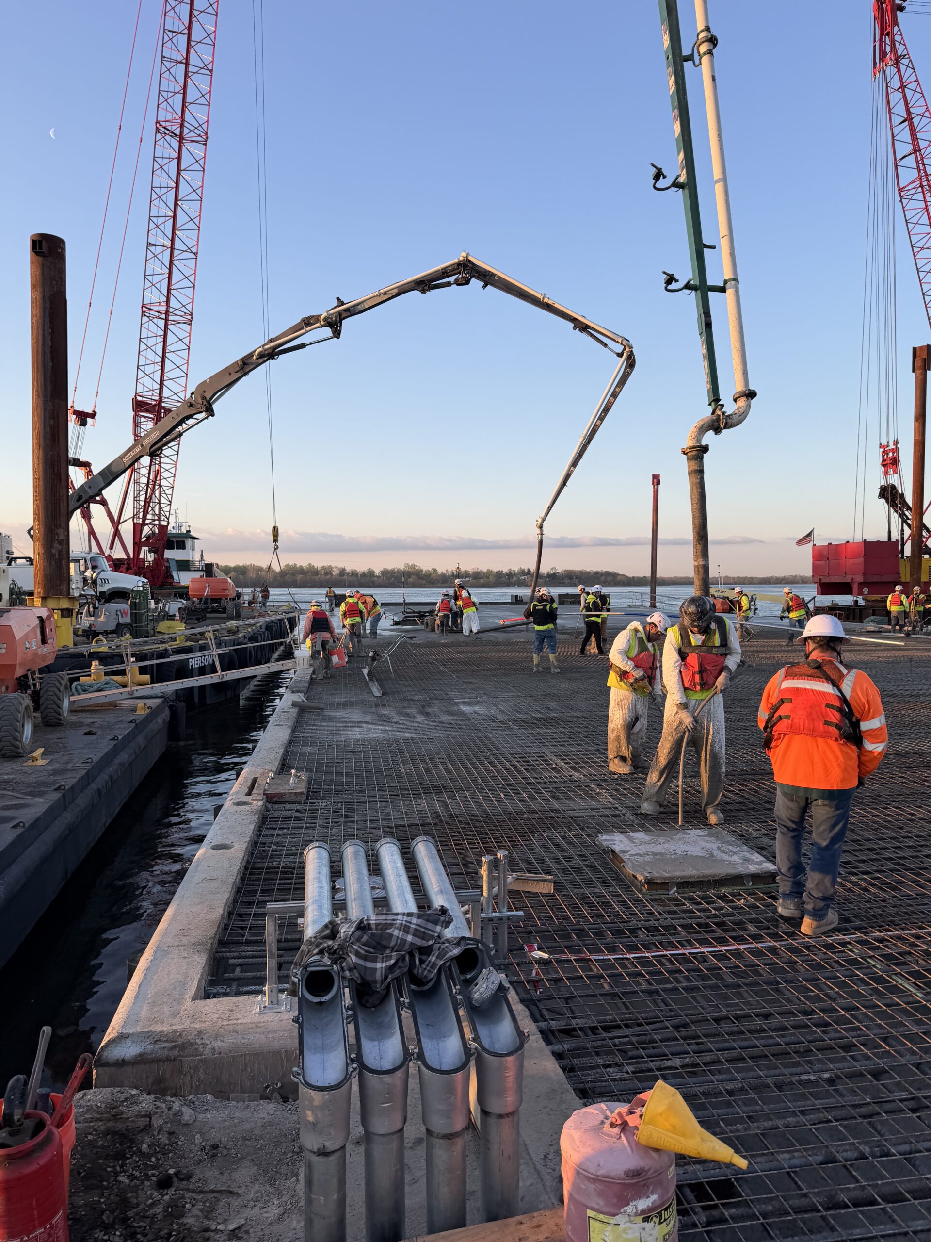 Crews placing the concrete pier deck at Pier 6A, Philadelphia Navy Yard, with a concrete pump boom and cranes over the Delaware River